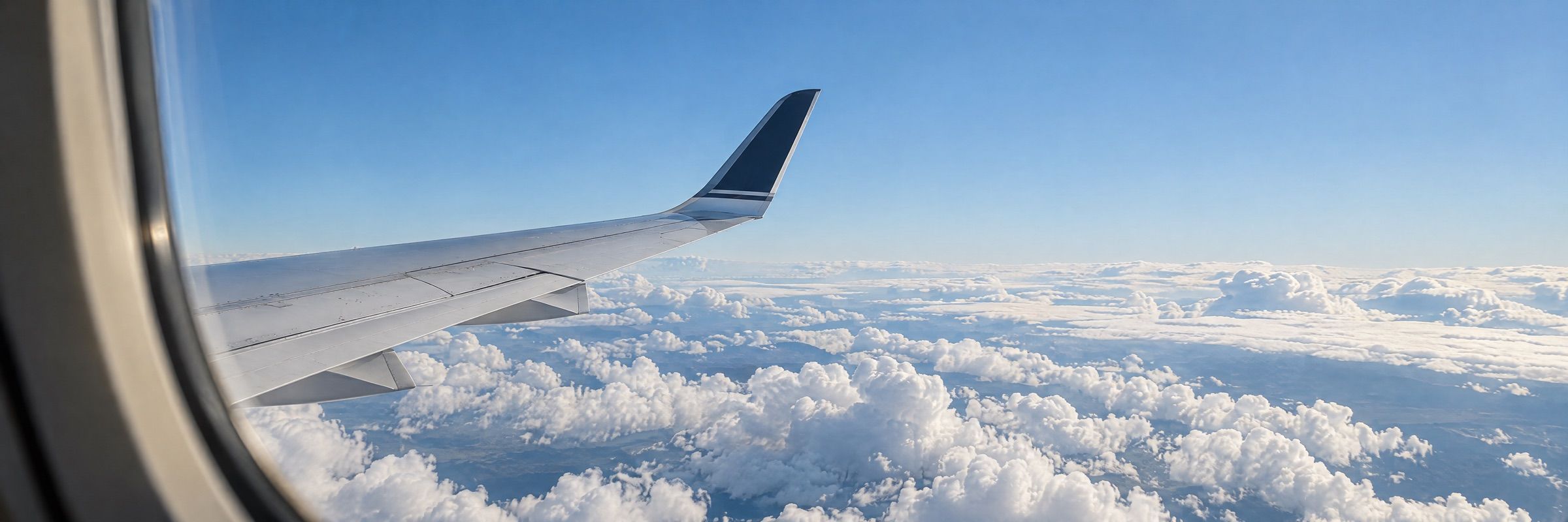 A jet’s wing and winglet above white cumulus clouds